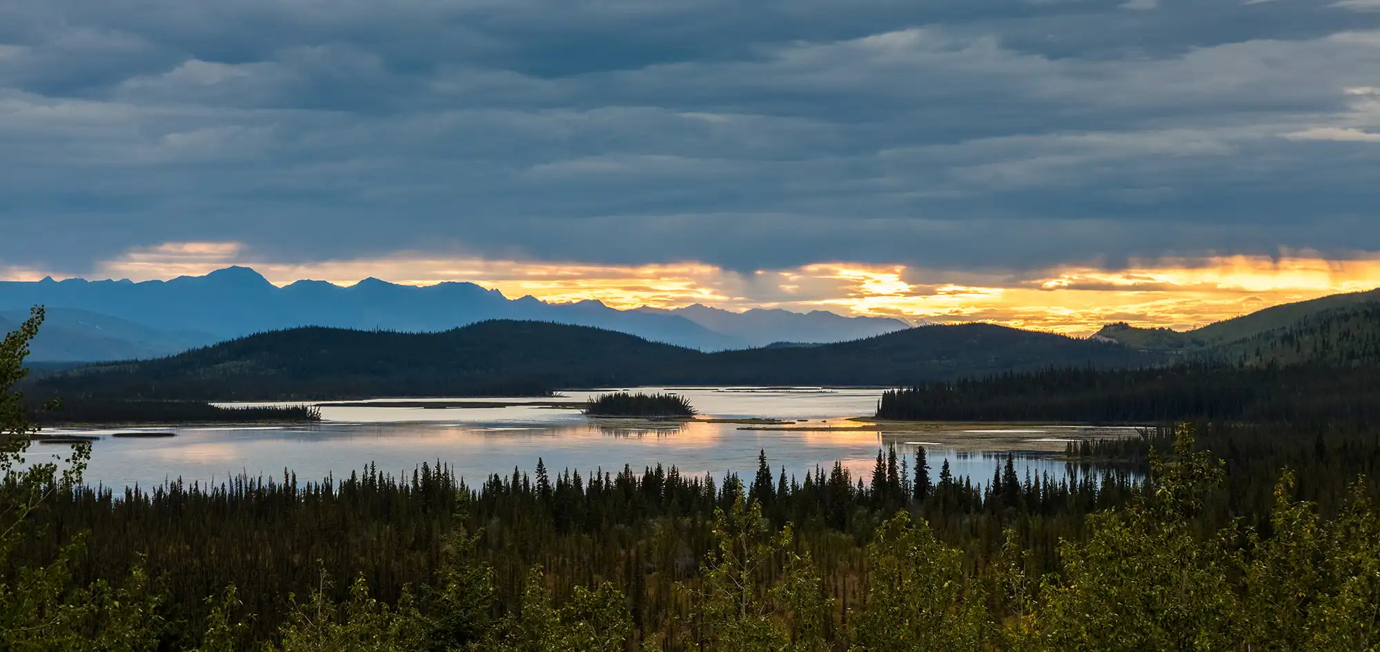 Scenic view of a lake with mountains and trees under a cloudy sky.