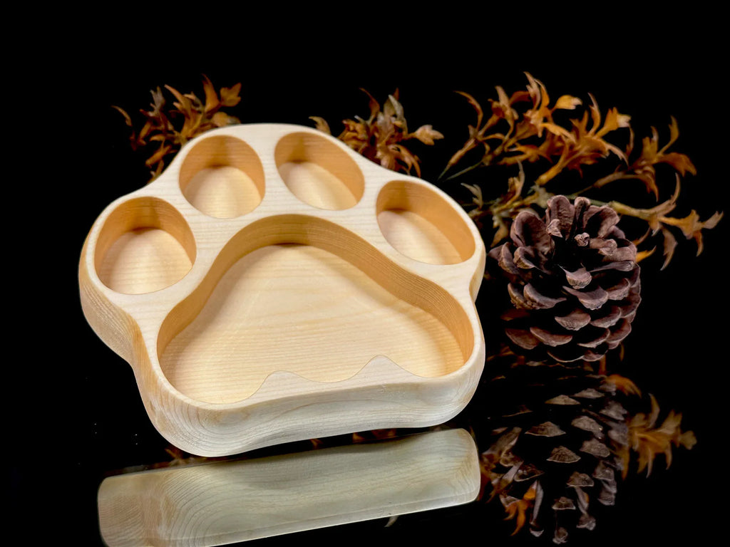 Wooden paw-shaped tray with pine cones and branches on a black background