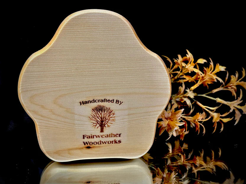 Wooden product with 'Fairweather Woodworks' branding on a reflective surface with flowers in the background.
