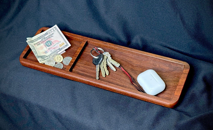 Wooden tray with money, coins, keys, and a white device on a dark blue fabric background